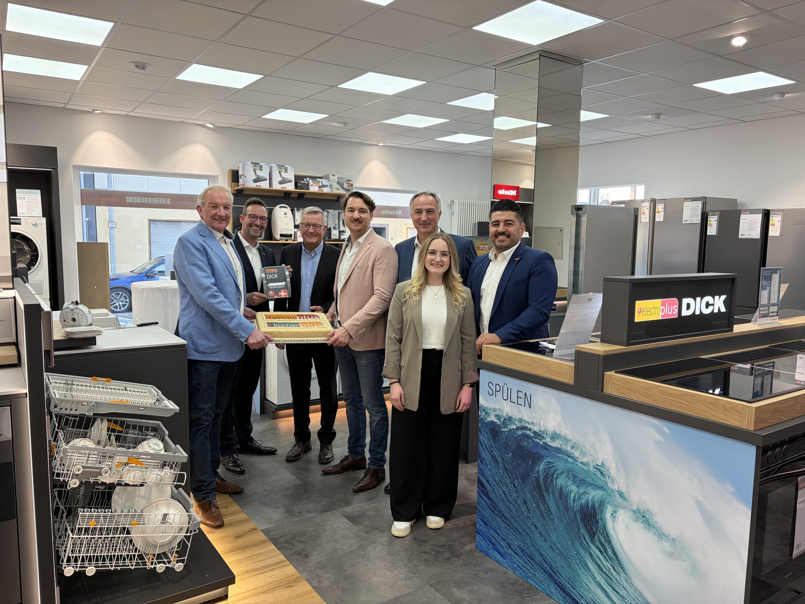 Tortenübergabe im Geschäft: (v.l.n.r.) Horst-Werner Dick (Inhaber, electroplus küchenplus Dick), Martin Wolf (General Manager EK Home Electrical Appliances, EK Retail), Joachim Müller (Mitglied der Geschäftsleitung, electroplus küchenplus Dick), Maximilian Dick (Geschäftsführer, electroplus küchenplus Dick), Christian Bichlmeier (Regionalleiter electroplus küchenplus, EK Retail), Pia Strieder (E Commerce Manager, EK Retail) und Ali Uyar (Store Designer electroplus, EK Retail).