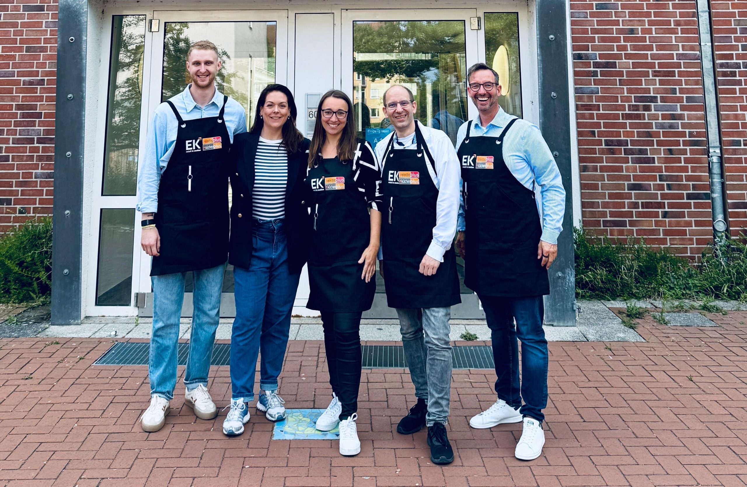 Vor der Schule: Gemeinsam für ein gutes Frühstück – electroplus küchenplus  unterstützt brotZeit e.V. (v.l.n.r.): Paul Süwer (Team Lead Marketing and Digital  Solutions, EK Retail), Verena Schmitt (Pressesprecherin, brotZeit e.V.), Meike Ull rich (Senior Concept Manager electroplus, EK Retail), Christian Claes (Senior  Concept Manager küchenplus, EK Retail) und Martin Wolf (General Manager EK  Home Electrical Appliances, EK Retail).